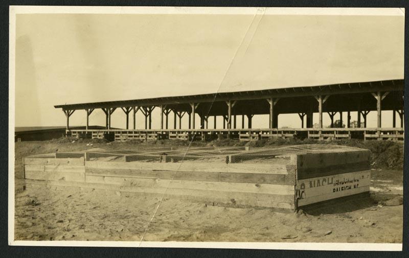 A sepia toned photo of a large wooden box at the NC State Fair Grounds. A large shelter stands in the background.