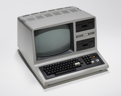 An early model computer with a large screen and attached keyboard sits on light gray background