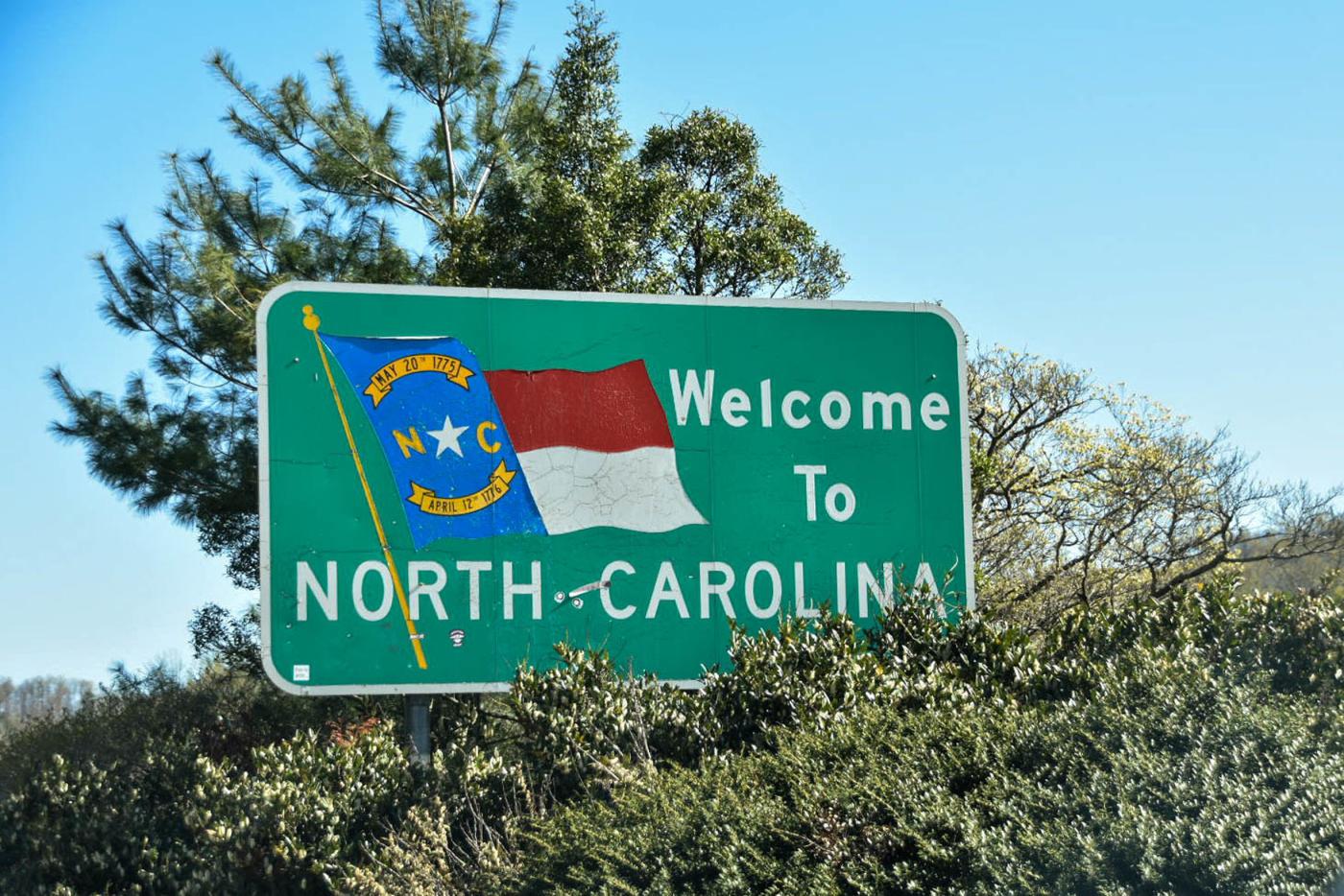 A sign that says Welcome to North Carolina surrounded by greenery and blue sky.