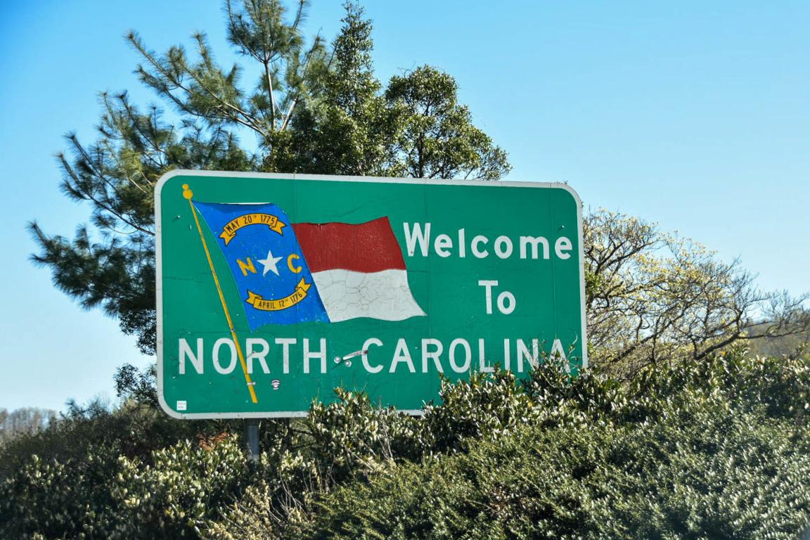 A sign that says Welcome to North Carolina surrounded by greenery and blue sky.