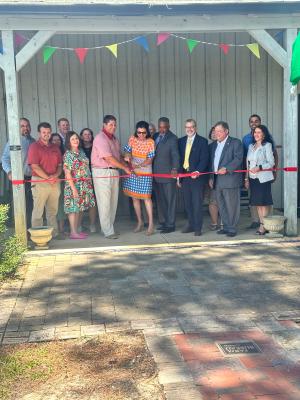 Group of people at a ribbon-cutting ceremony under a pavilion with colorful flags.