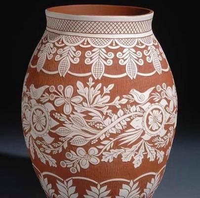 A handcrafted clay pot with intricate white etchings of floral and geometric patterns on a reddish-brown surface
