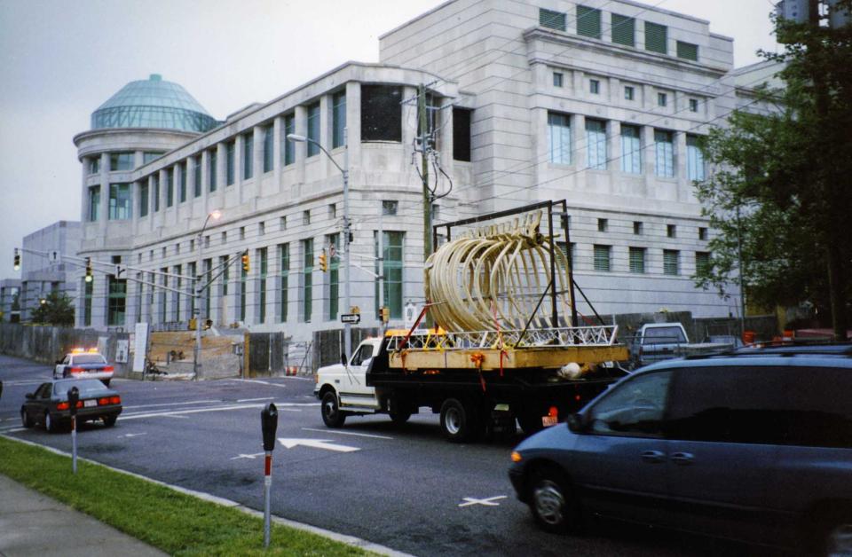 Wide shot of downtown Raleigh, where a flatbed truck drives with whale ribs on the back.