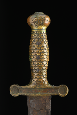 Close-up of a brass sword hilt with scale-patterned grip and eagle engraving on the pommel.