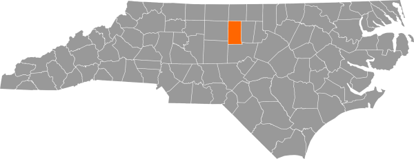 A gray map of North Carolina with Alamance County filled in with orange.