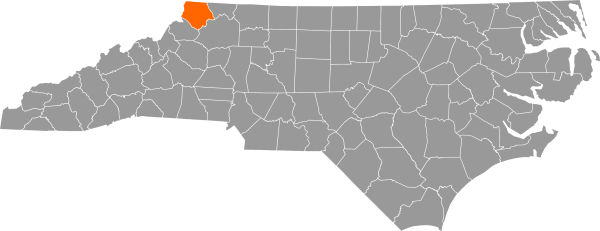 A gray map of North Carolina with Ashe County filled in with orange.