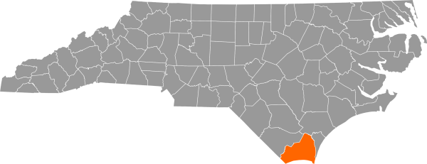 A gray map of North Carolina with Brunswick County filled in with orange.
